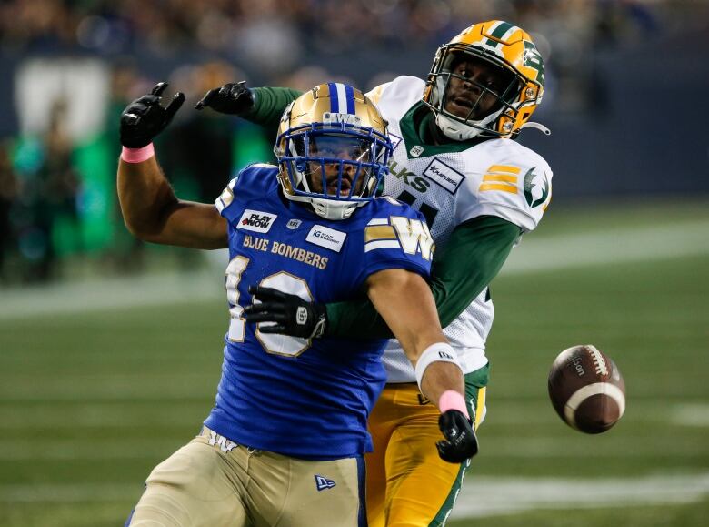 A player in a blue jersey loses the football while a player in a white jersey runs into him.