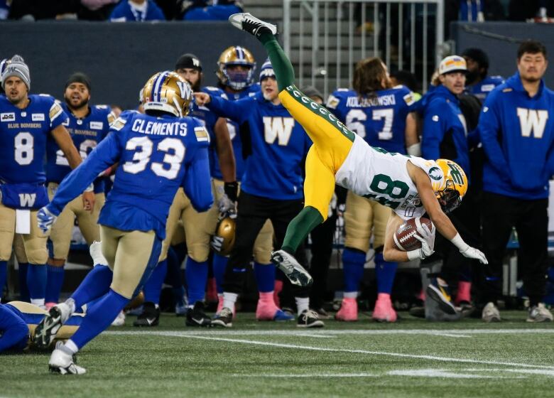 A player in a blue jersey runs behind a player in a white jersey who's falling in the air as he holds the football.