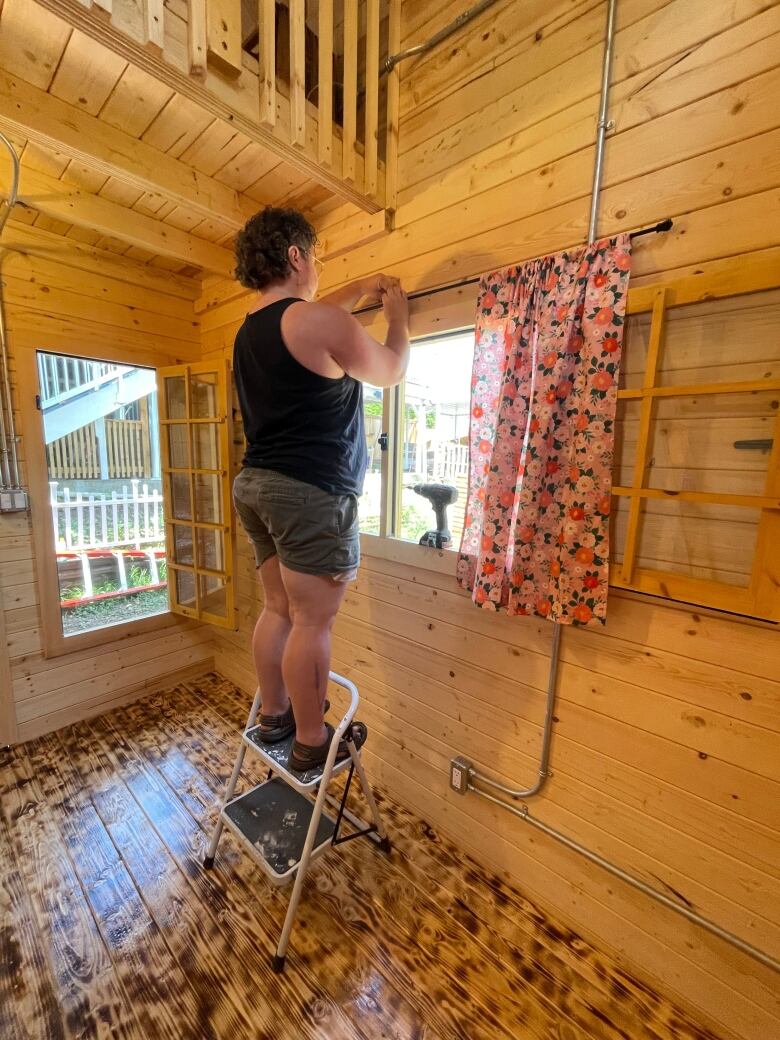 A man hangs up curtains in a wooden cabin.