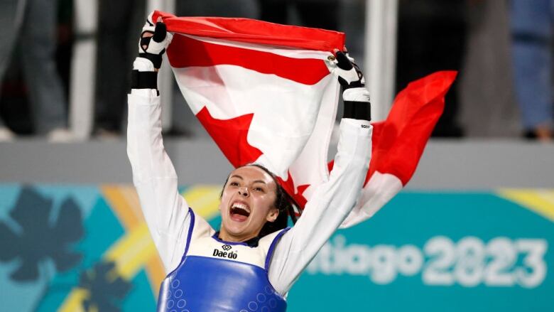 A female taekwondo competitor holds up a Canadian flag after winning a gold medal at the Pan Am Games.