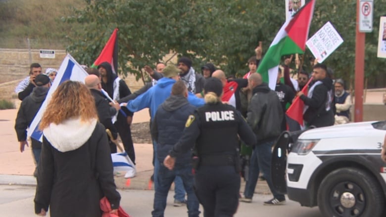 Police rush into a scene where people are yelling at each other and holding flags