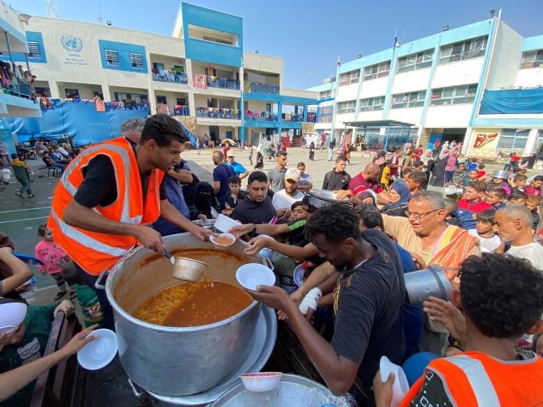 Man in orange security vest hands out food to people in lot 