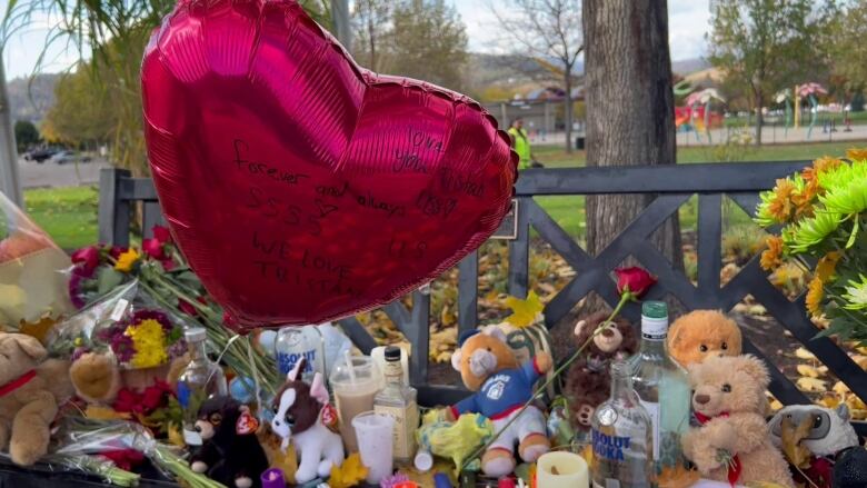 Teddy bears, a balloon and various bottles litter a park bench.