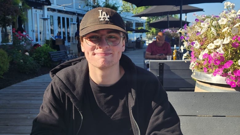 A teenage boy with a baseball cap smiles while sitting down.