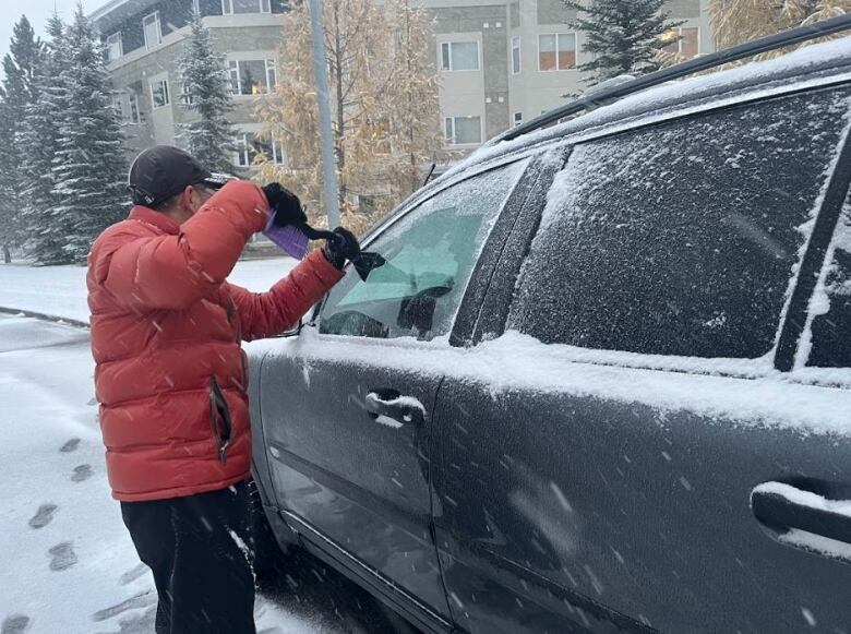 A person scrapes the window of their black car.