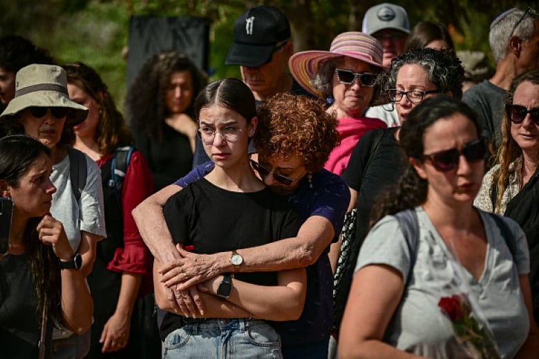 A teenage girl cries as she stands in a crowd. A woman behind her wraps her arms around her.