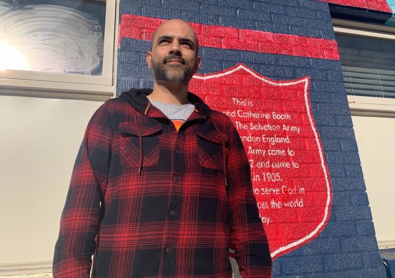 A man stands outside a mural on a building in Saskatoon.