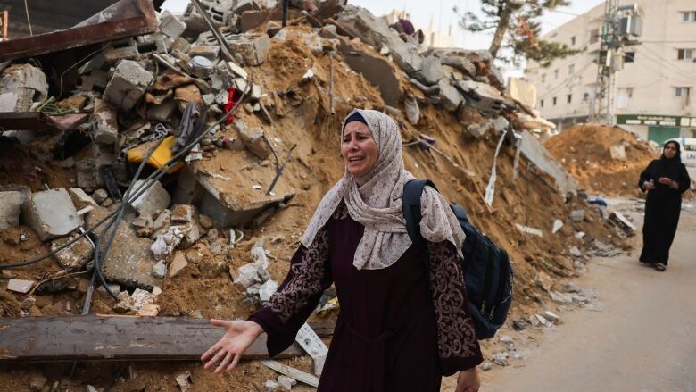 A person reacts while standing next to the rubble of a destroyed building.