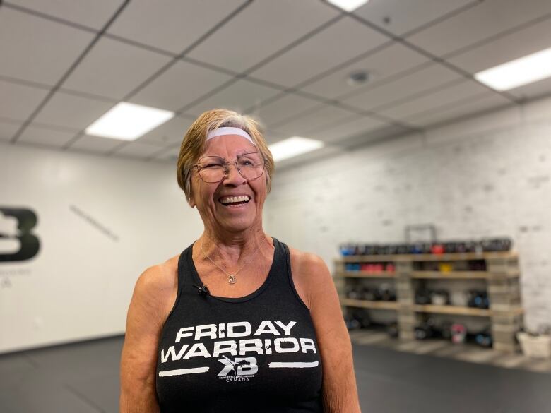 person is standing up wearing a dark muscles shirt and head band, while smiling.