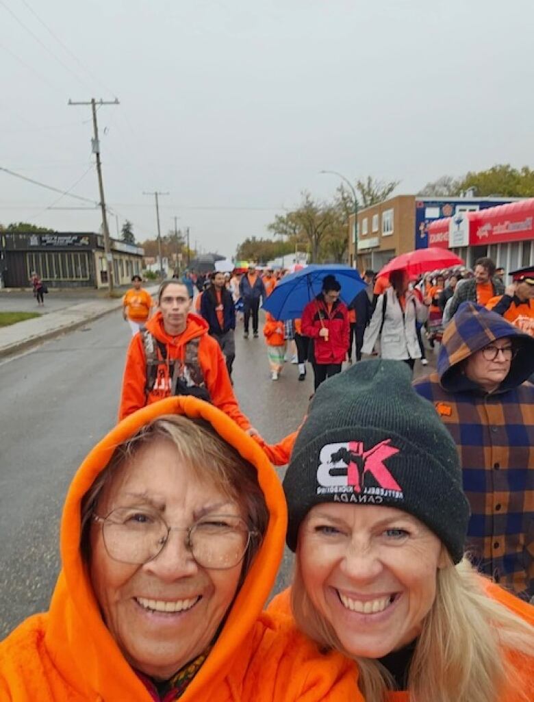 two people close together wearing bright clothing, one is swearing a hooded sweatshirt with glasses and the other is wearing a dark toque.