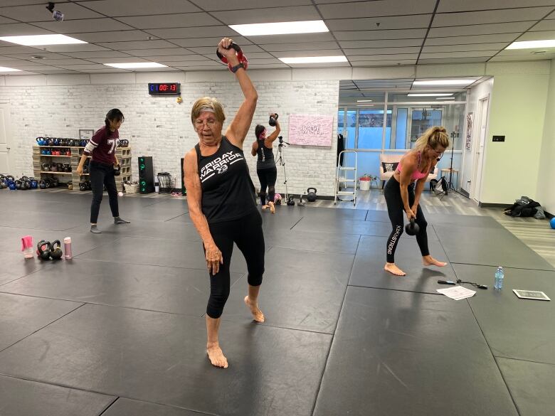 person is swearing dark clothing while wearing a headband and glasses, as they hold a weight in the air.