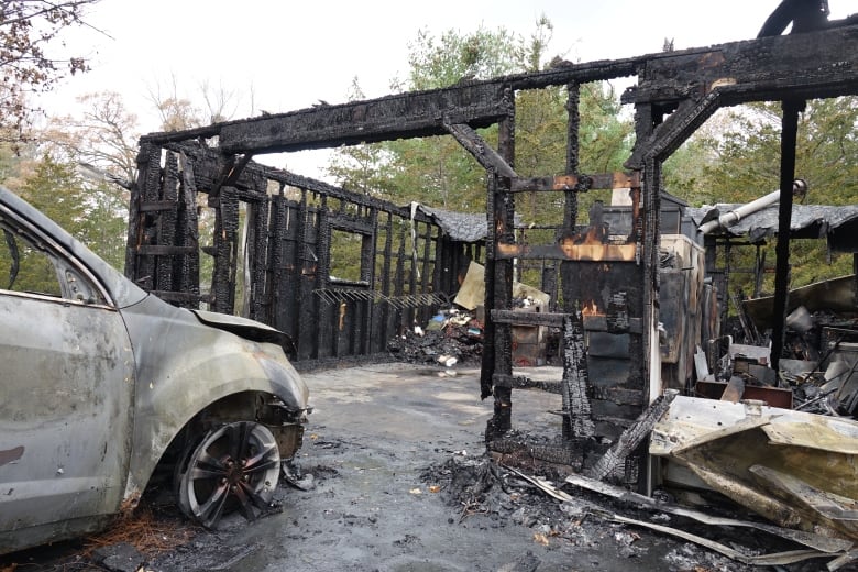 A white vehicle that's heavily scorched can be seen in the foreground. It's front tire is melted off and it's paint has peeled away because of the heat. In front of it is the charred skeleton of a garage.