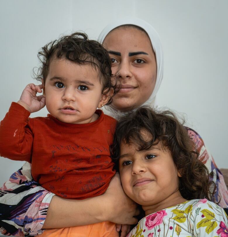 A seated woman holds two young girls.