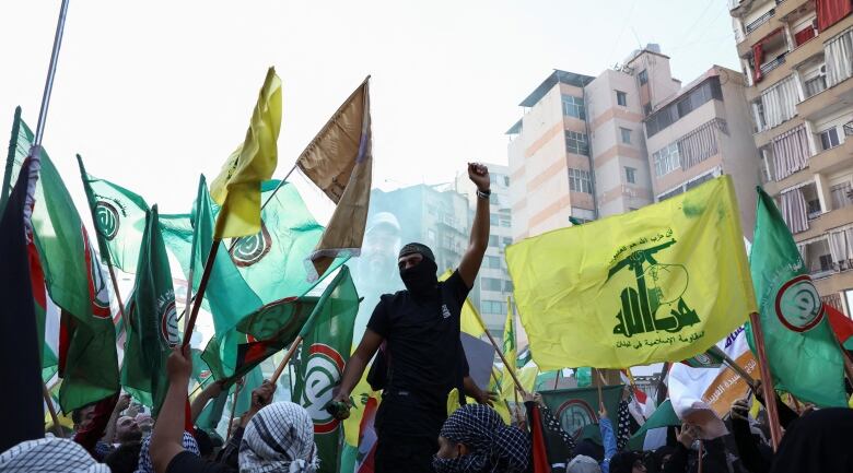 A large group of demonstrators, some masked, raise flags and their fists during a protest on a city street. 