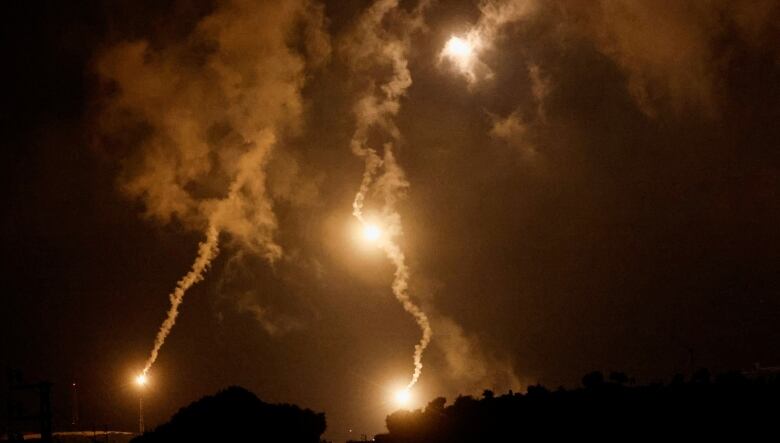 Three large flares, trailing smoke, fall at night. 