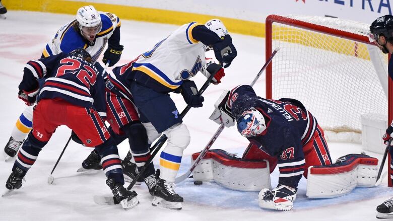 Four players jostle in front of the crease while the puck lies against the right pad of the Winnipeg Jets goalie.