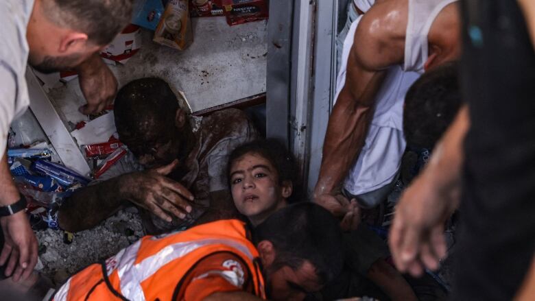 A man in an orange reflective vest and other people are shown in a cramped site filled with debris.