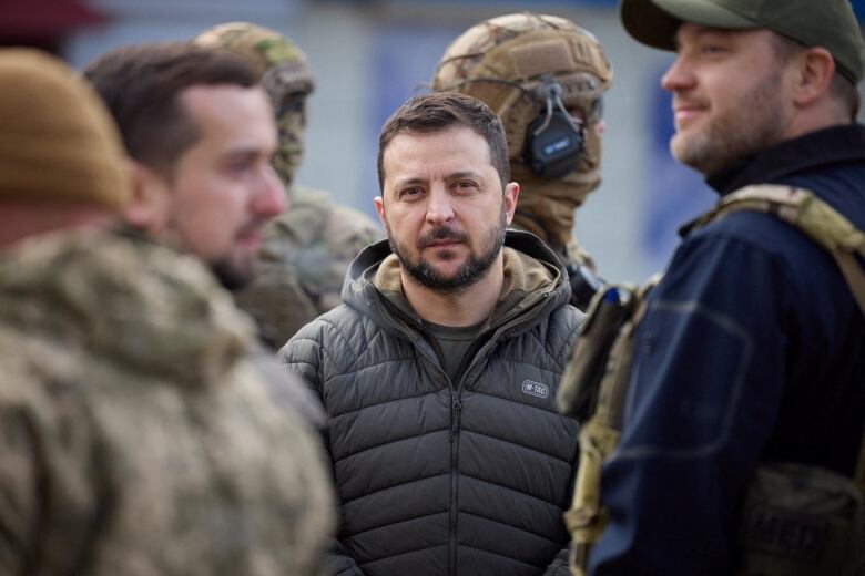 A man in a green puffer jacket stands in a crowd.