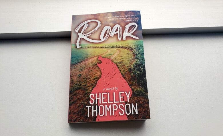 A book titled ROAR with a pink silhouette of a bear standing tall in front of a field on the cover.