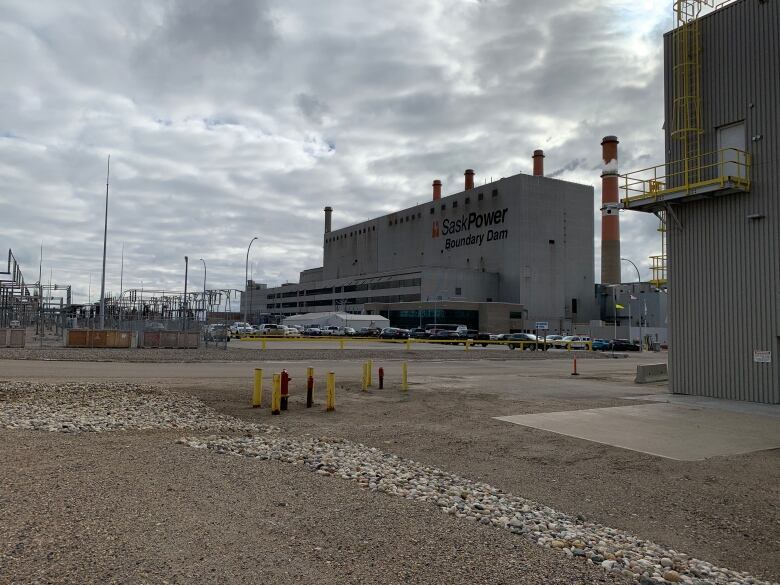 A power plant sits in the distance near a gravel parking lot.