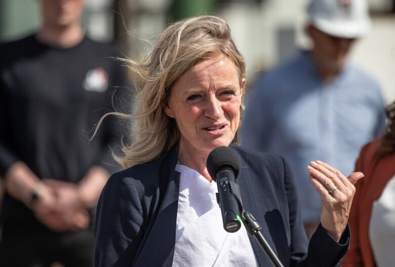 A woman talks to an outdoor crowd with the wind blowing her hair.