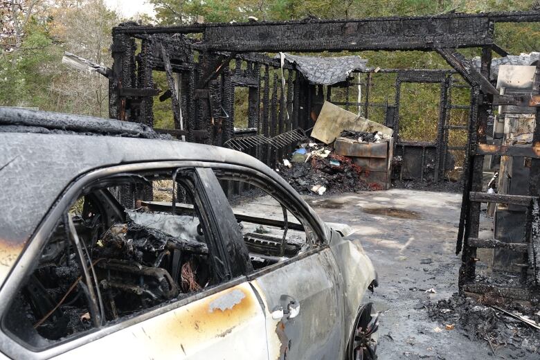 A white vehicle that's heavily scorched can be seen in the foreground. It's front tire is melted off and it's paint has peeled away because of the heat. In front of it is the charred skeleton of a garage.