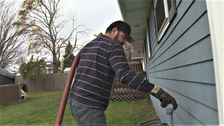 Man delivers heating oil to a pipe outside a house.