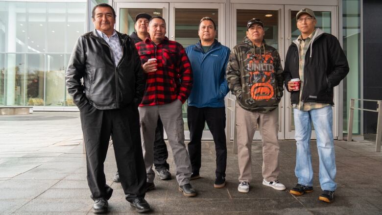 Six men stand outside of a building.