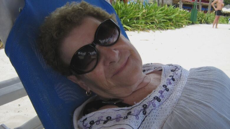 A woman wearing sunglasses reclines in a beach chair.