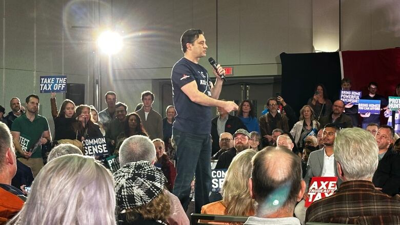 A crowd stands around a man wearing a navy t-shirt.