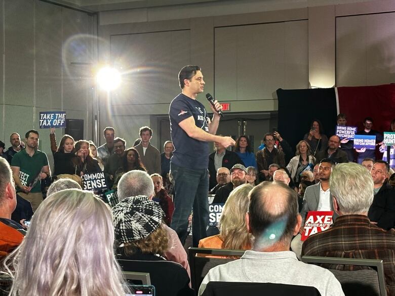 A crowd stands around a man wearing a navy t-shirt.