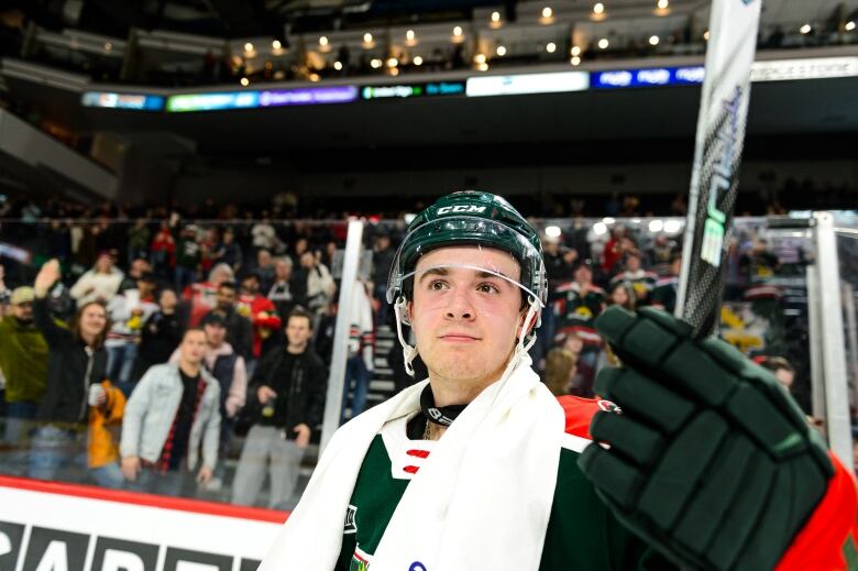 A hockey player tips his stick to the crowd, who are shown cheering him on.