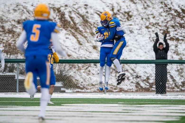 Two football players in blue uniforms jump while hugging.