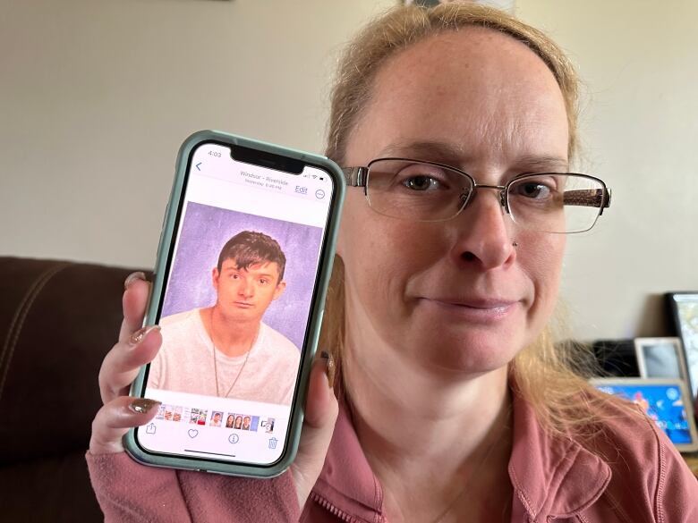 A woman holds a cellphone showing a pic of a teenage boy.