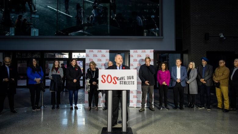 A press conference with man in front standing in the podium with other people standing behind him. 