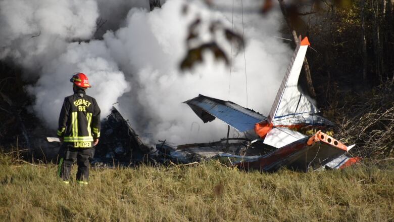 A plane spews smoke on the ground while a firefighter looks on.