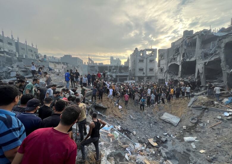 A crowd of people are seen amid the rubble of destroyed buildings.