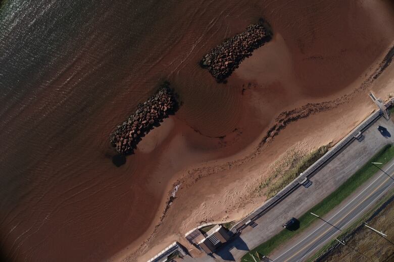 Two piles of rocks on a shoreline next to a road 