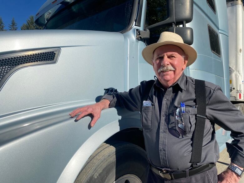 A white man wearing a Panama hat poses while hanging off a truck.