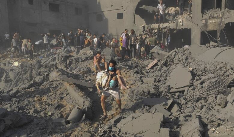 A person carries a body through rubble.