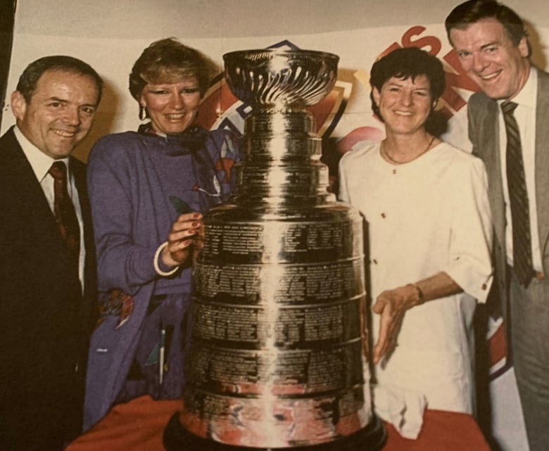 Four people pose with the Stanley Cup in between them.