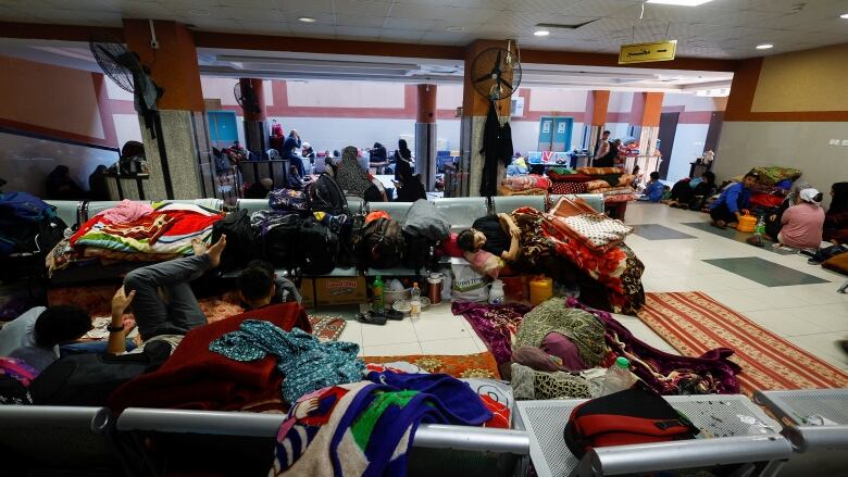 A hospital waiting room with a number of people lying down under blankets.