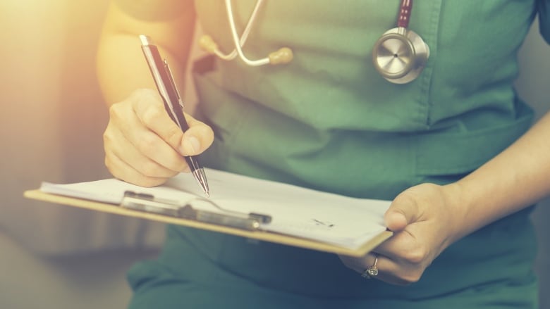 A stock photo of a nurse holding a clipboard and wearing scrubs.