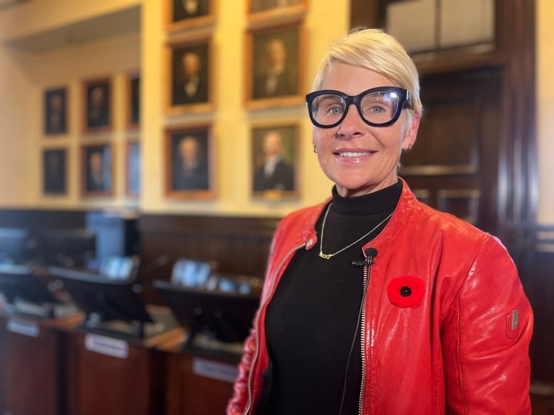 A woman in a red leather jacket and black glasses standing inside council chambers in Charlottetown.