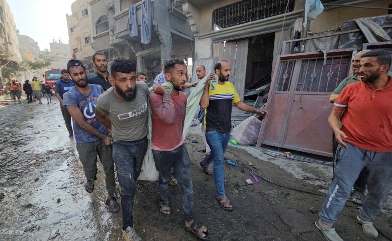 Several men walk on muddy ground carrying a sack that is believed to contain the body of a person.