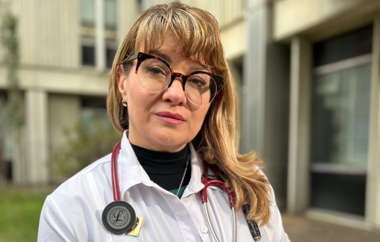 Female physician in white coat and stethoscope standing outside.