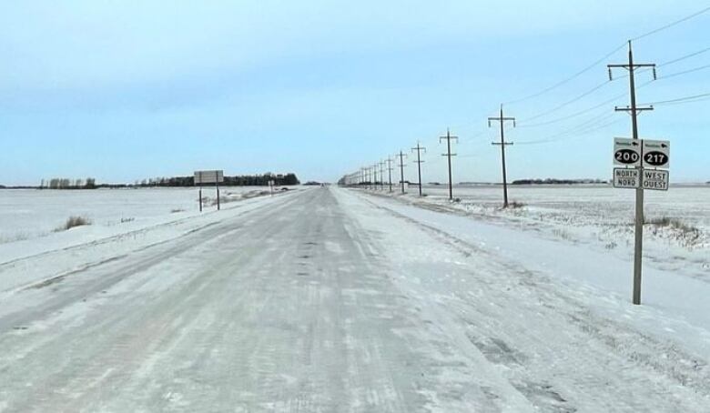 An icy highway is seen surrounded by snow-covered prairie fields.