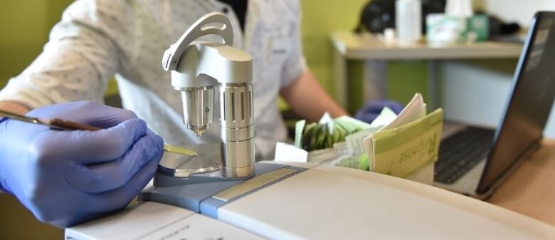 A person in blue rubber gloves places a substance on a plate underneath a steel testing device.