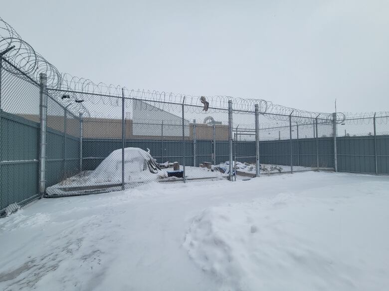 A snow-covered sweat lodge is seen penned in by a barbed wire prison fence.