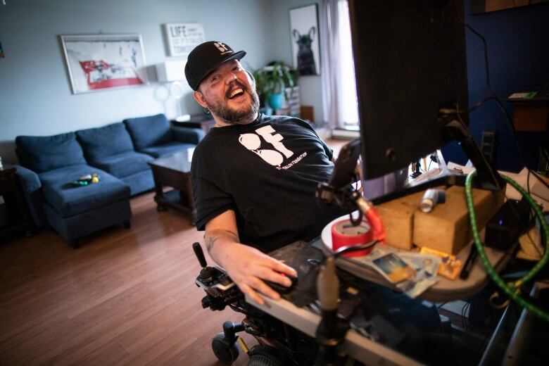 A man in a wheelchair laughs at his desk at home.